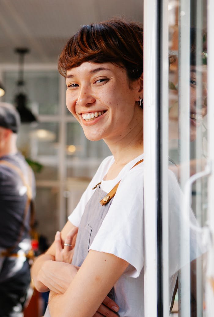 Cheerful barista with crossed arms smiling confidently in a bustling modern café.