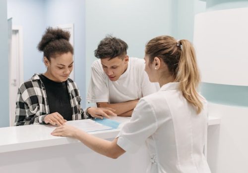 a-medical-staff-in-a-clinic-7108317 A nurse assists two patients at a hospital reception, emphasizing healthcare service.